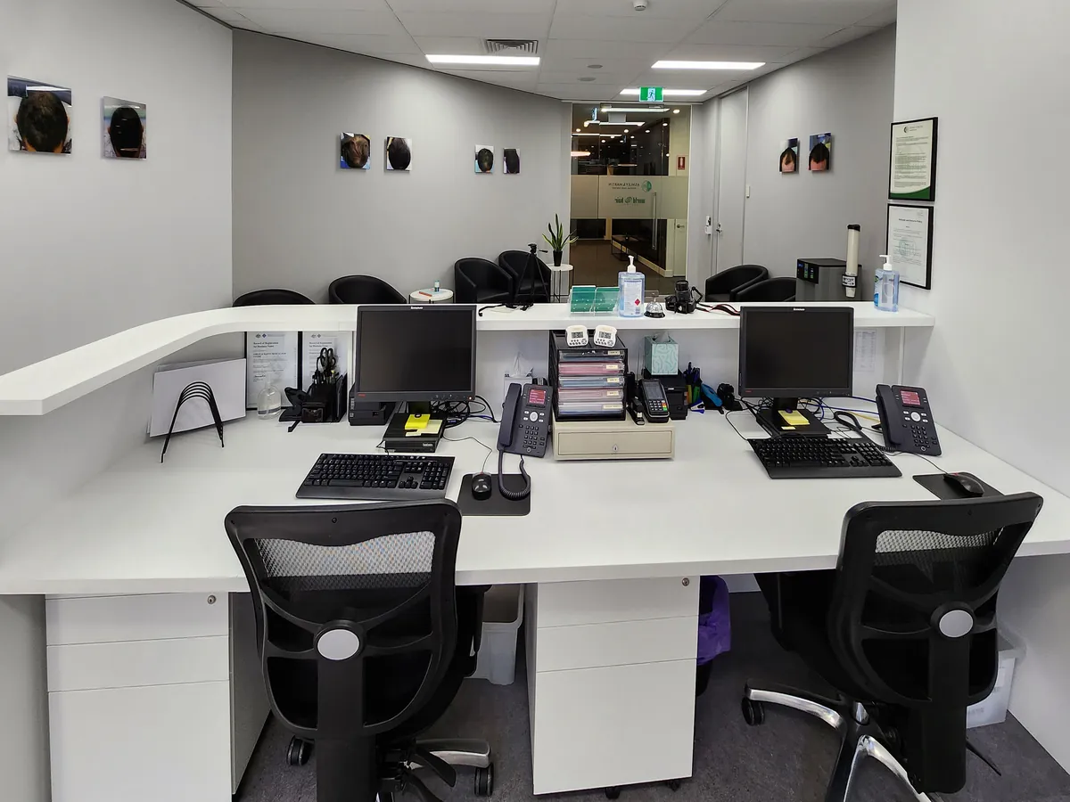 Behind the reception desk showing twin workstations and glazed entry at the Ashley & Martin cosmetic clinic fitout, Southbank.