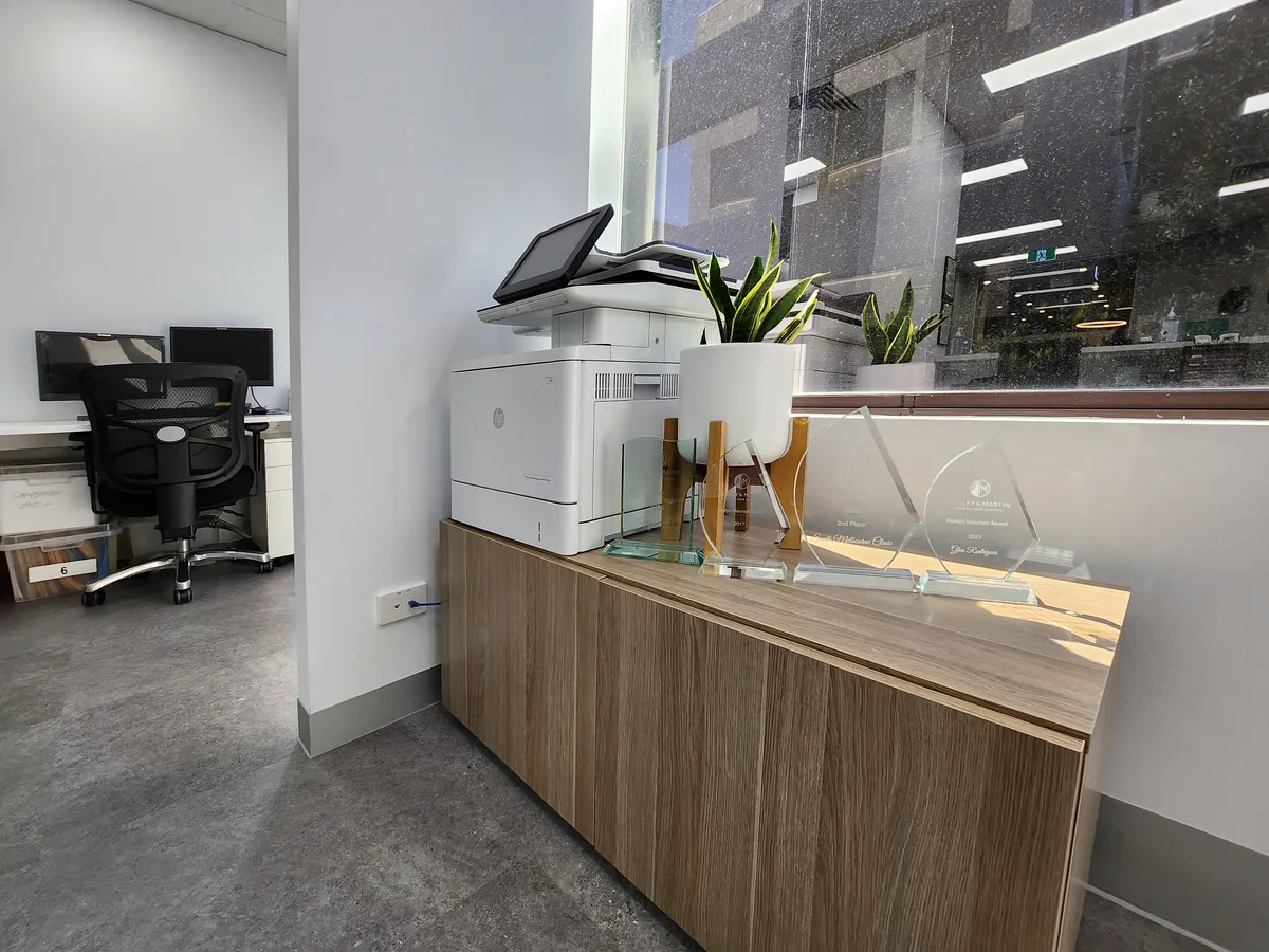 Timber reception credenza with printer and award trophies beside a back office at the Ashley & Martin cosmetic clinic fitout, Southbank.