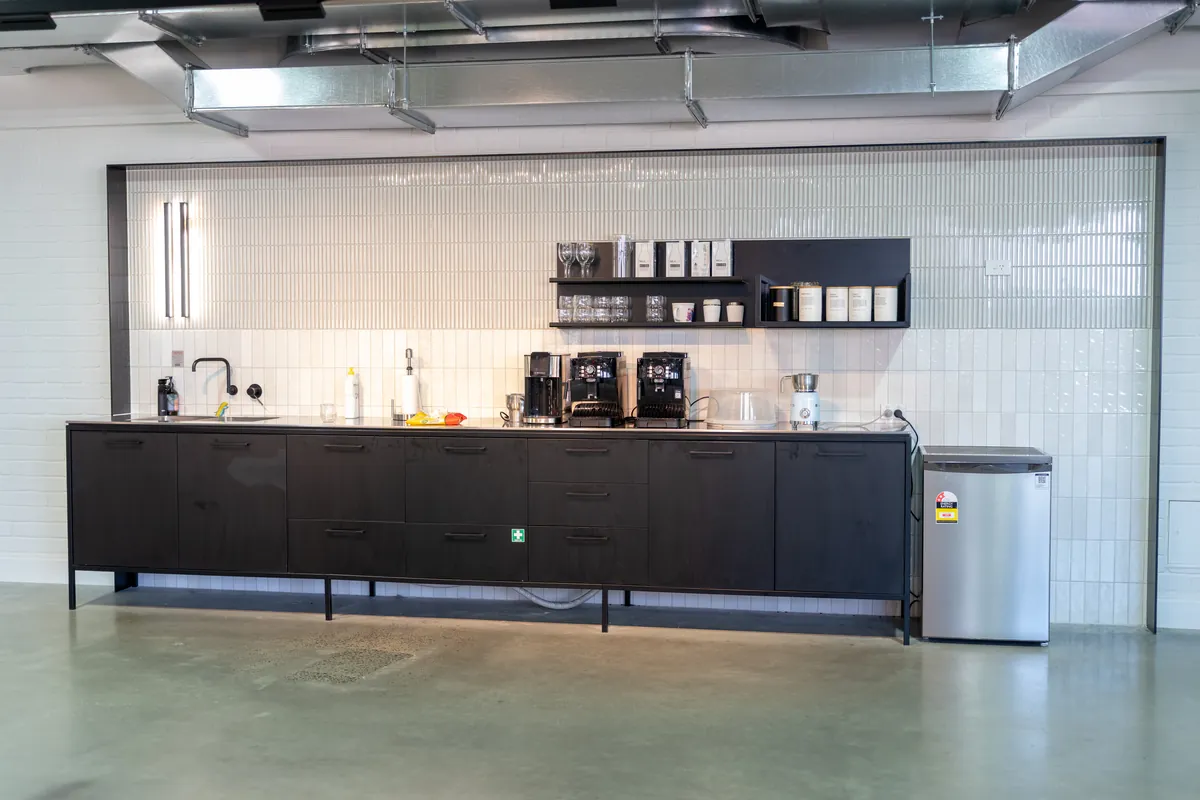 Black joinery kitchen with tiled splashback and coffee station, Clinibase office fitout, Collingwood.