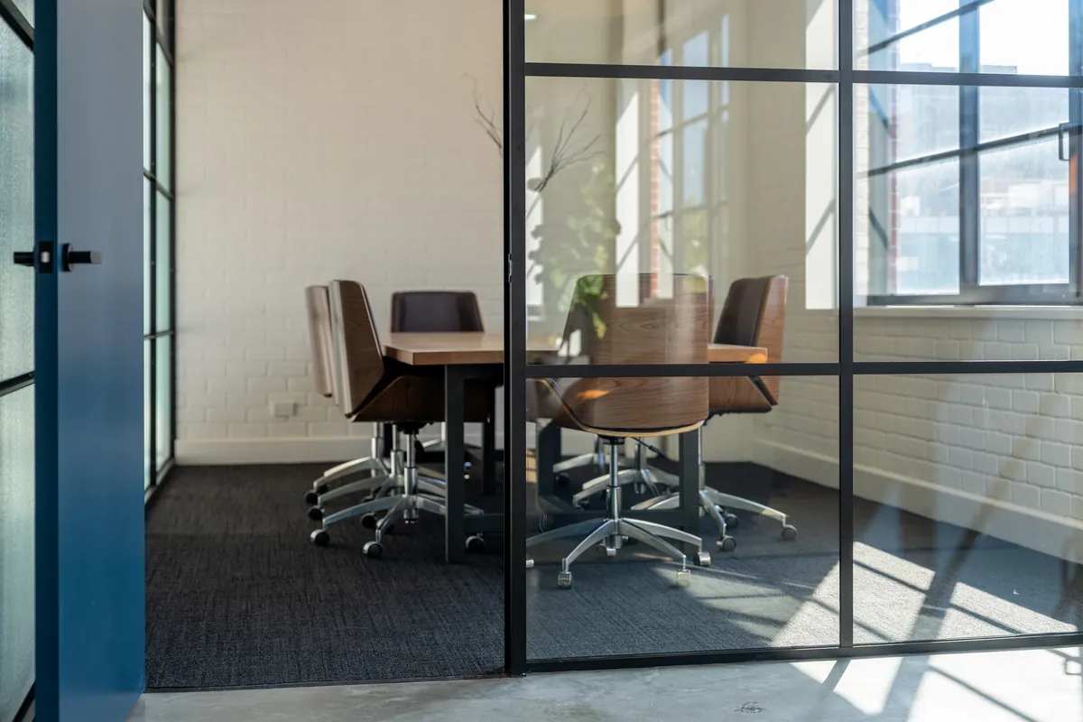 Boardroom-style meeting room behind black-framed glass partitioning, Clinibase office fitout, Collingwood.
