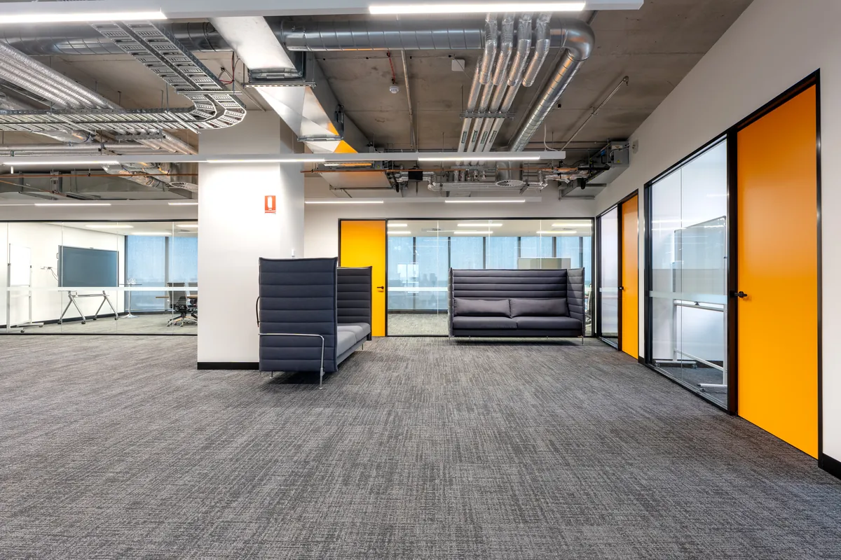 Open breakout zone with lounge seating, exposed services and meeting rooms at the Empower Wealth office fitout, North Melbourne.