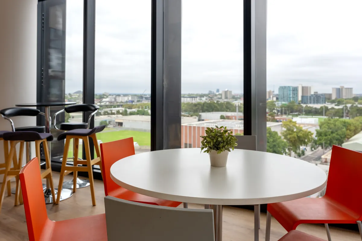 Breakout dining nook with red chairs, round table and city views at the Empower Wealth office fitout, North Melbourne.