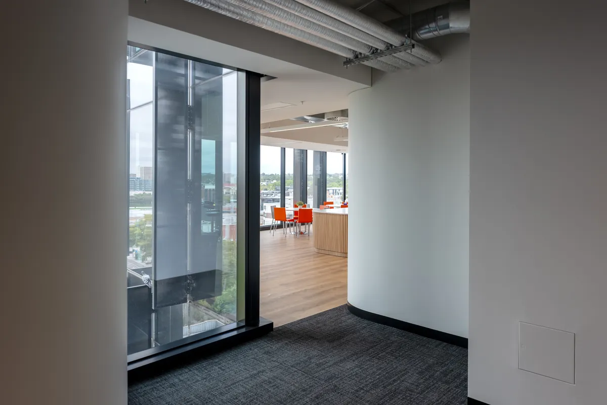 Curved corridor opening onto a breakout dining area with city views at the Empower Wealth office fitout, North Melbourne.