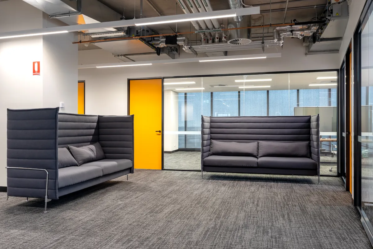 Breakout area with acoustic high-back lounges and a yellow feature door at the Empower Wealth office fitout, North Melbourne.