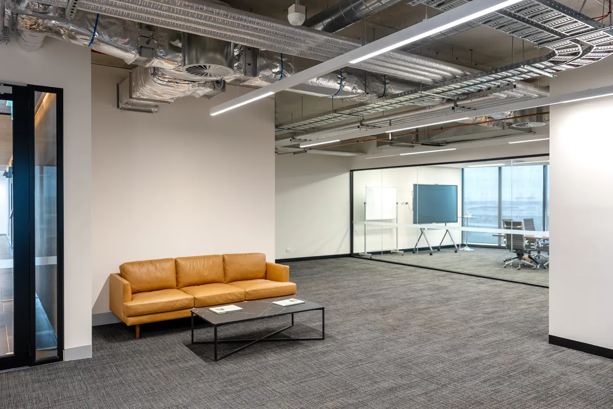 Breakout lounge with leather sofa beside a glass-walled meeting room at the Empower Wealth office fitout, North Melbourne.