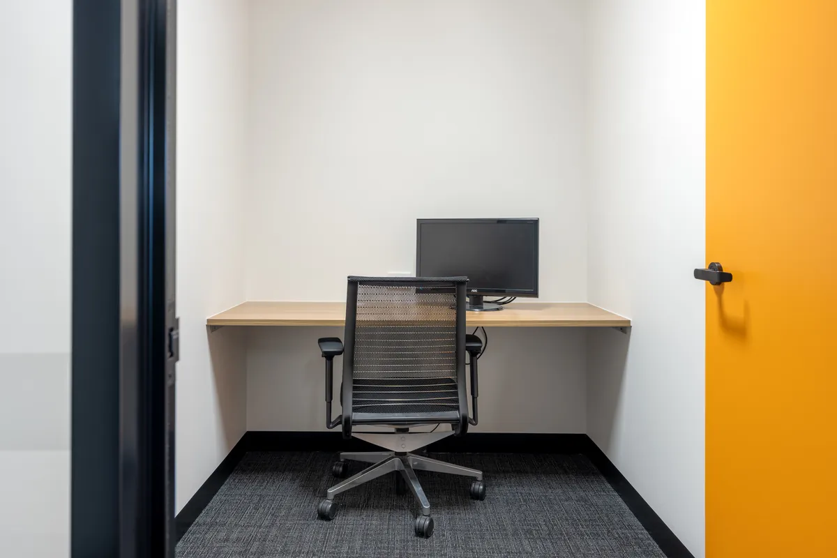 Single-person focus room with wall-mounted desk and yellow feature door at the Empower Wealth office fitout, North Melbourne.