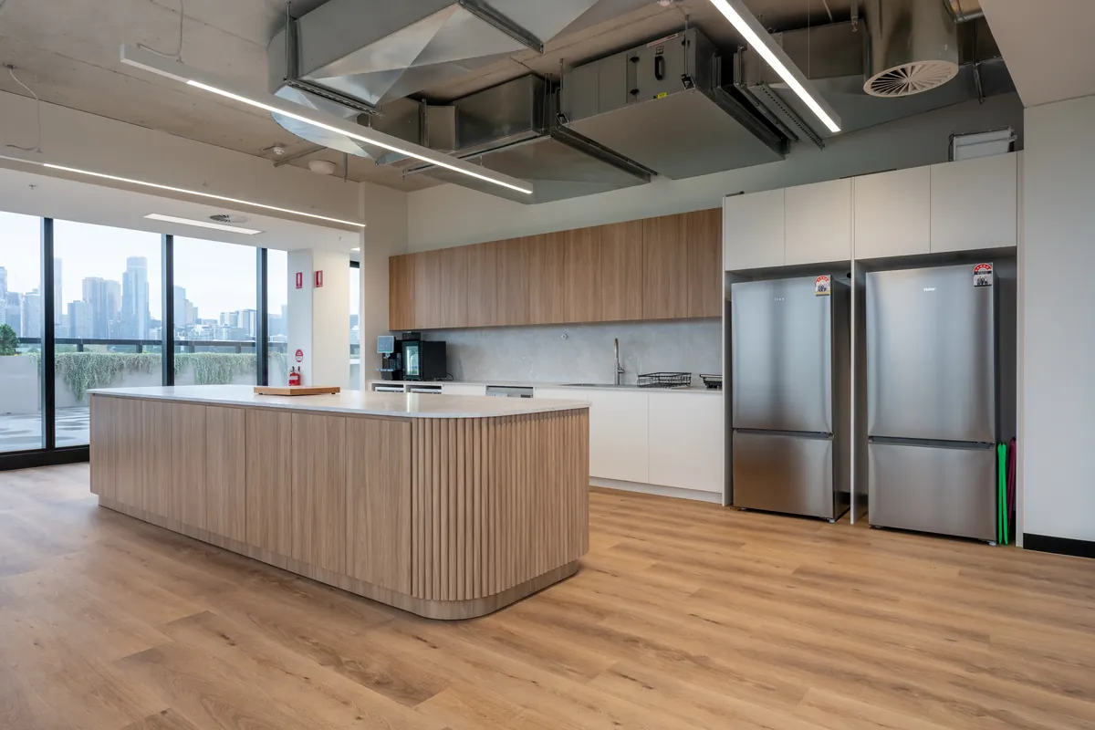 Office kitchen with fluted timber island, stone benchtops and twin fridges at the Empower Wealth office fitout, North Melbourne.
