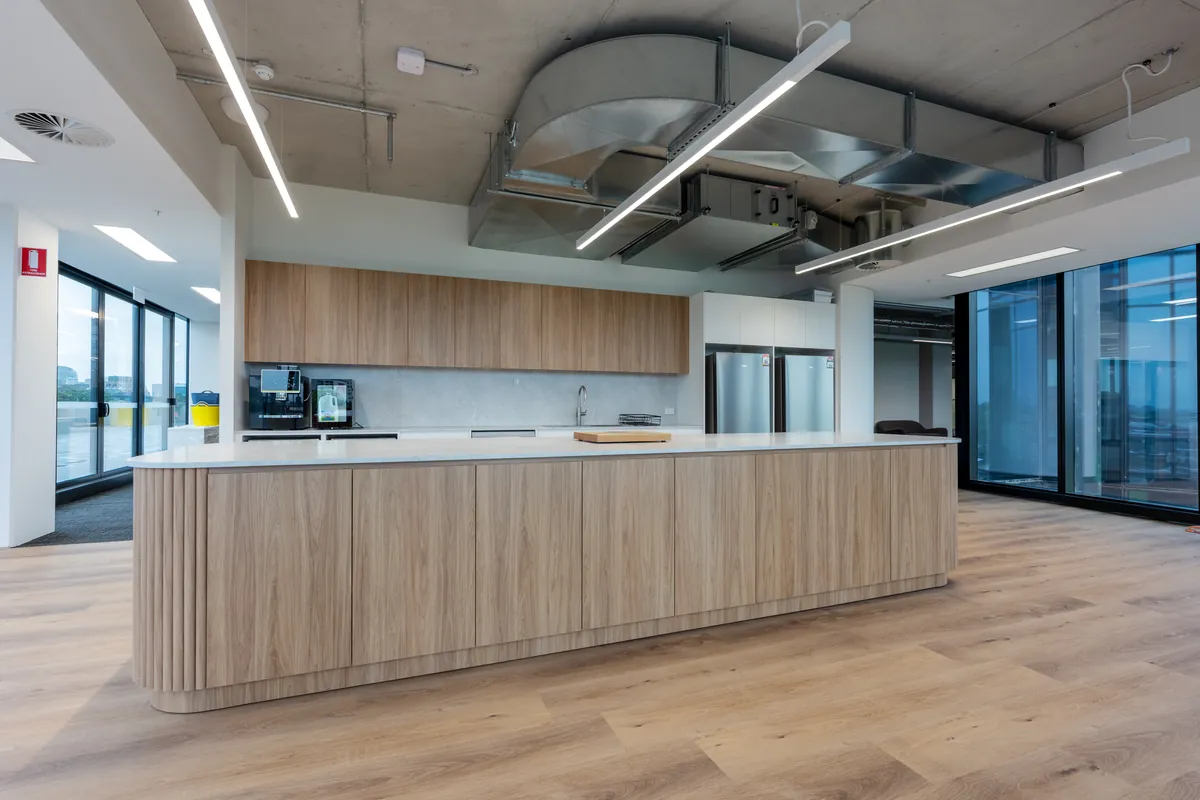 Curved fluted timber kitchen island with stone benchtop and exposed services at the Empower Wealth office fitout, North Melbourne.