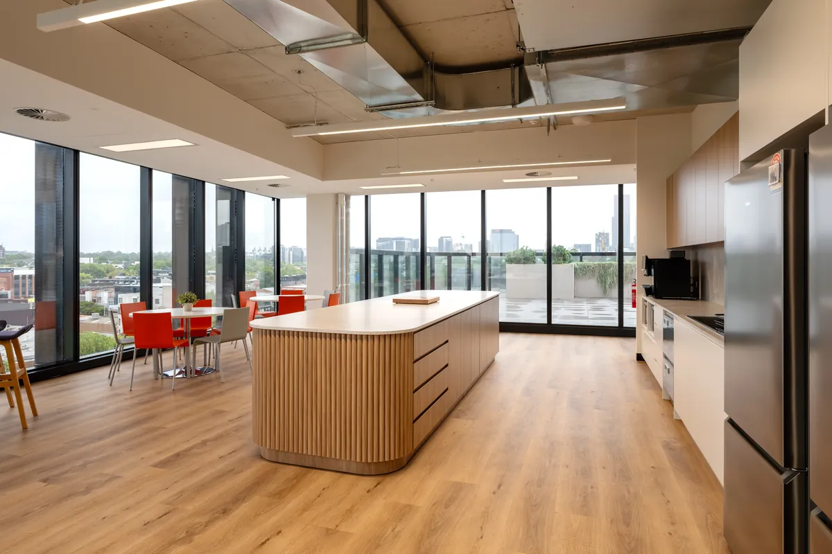 Kitchen and dining area with curved timber island bench and city views at the Empower Wealth office fitout, North Melbourne.