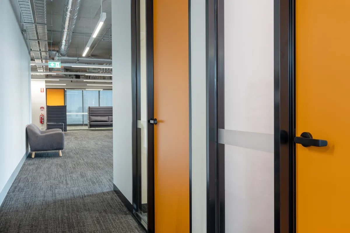 Acoustic meeting room doors with yellow framing and breakout lounge beyond at the Empower Wealth office fitout, North Melbourne.