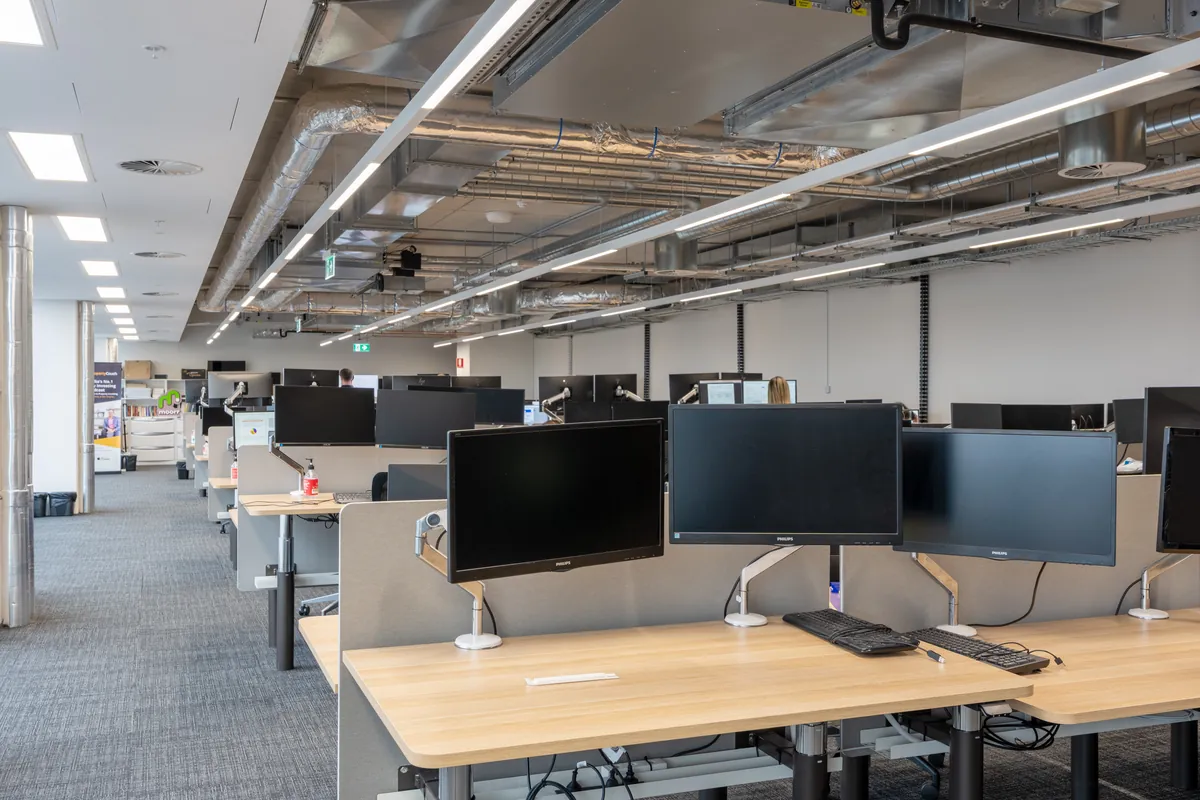 Rows of workstations with dual monitors and exposed ceiling services at the Empower Wealth office fitout, North Melbourne.
