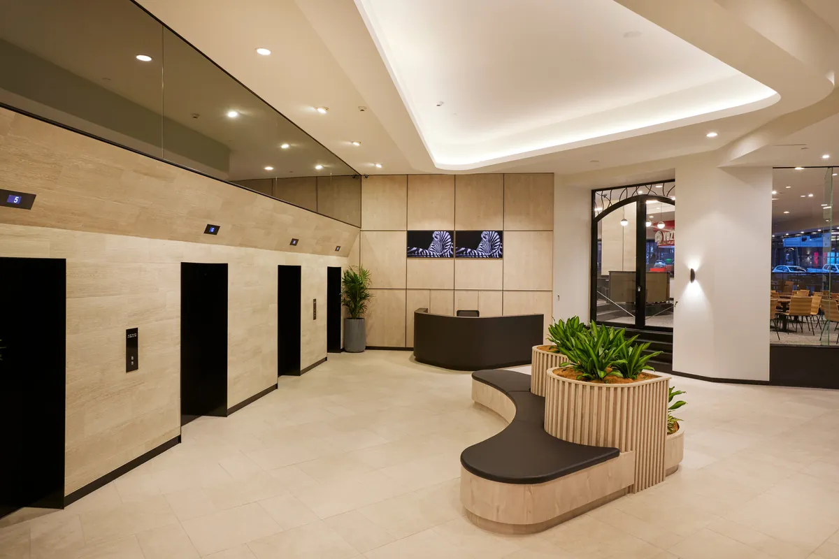 Lift lobby with travertine walls, curved planter seat and digital display at the Exchange Tower refurbishment, Melbourne.