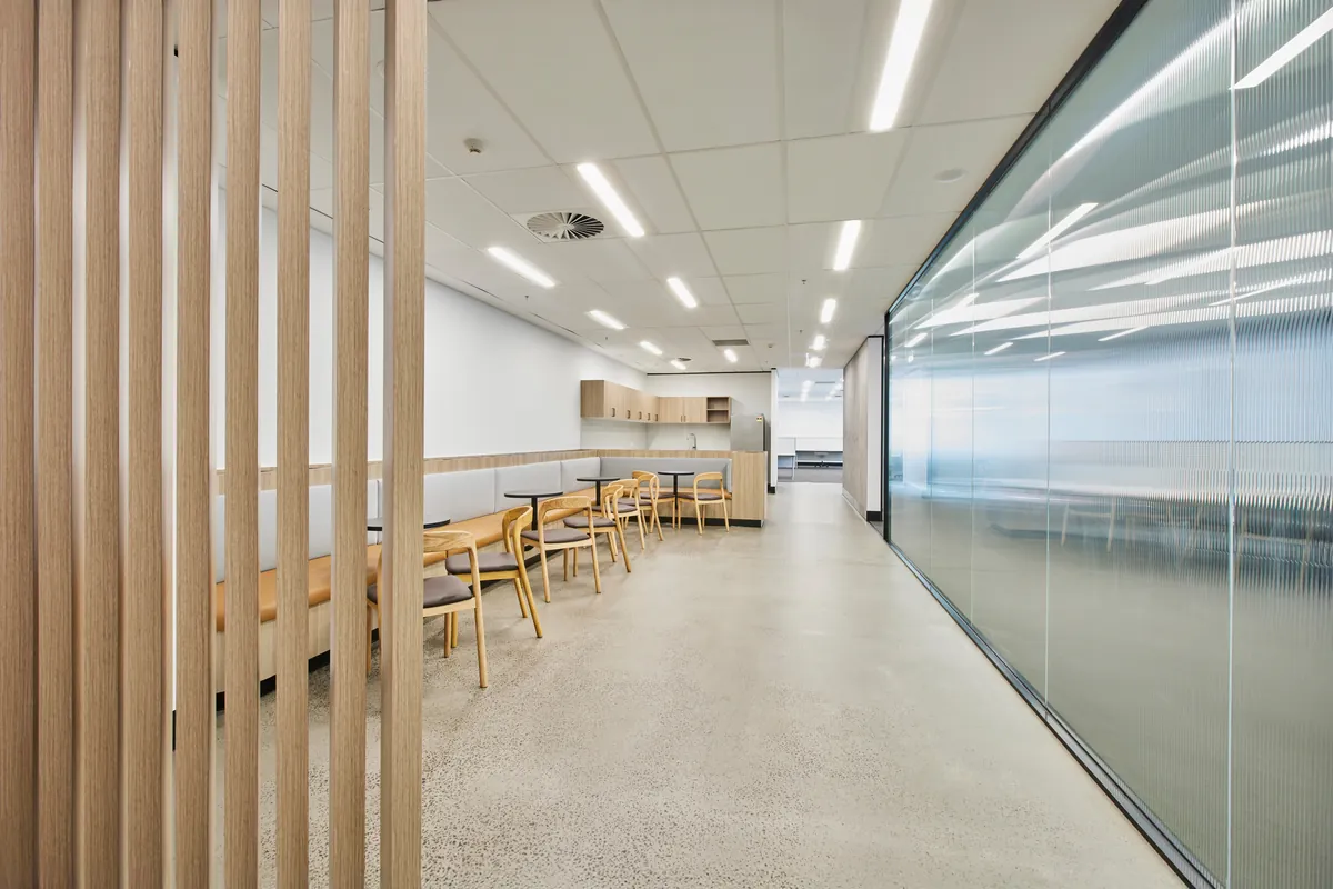 Breakout dining with timber slat divider and kitchenette behind fluted glass, Growthpoint spec suite fitout, Mulgrave.