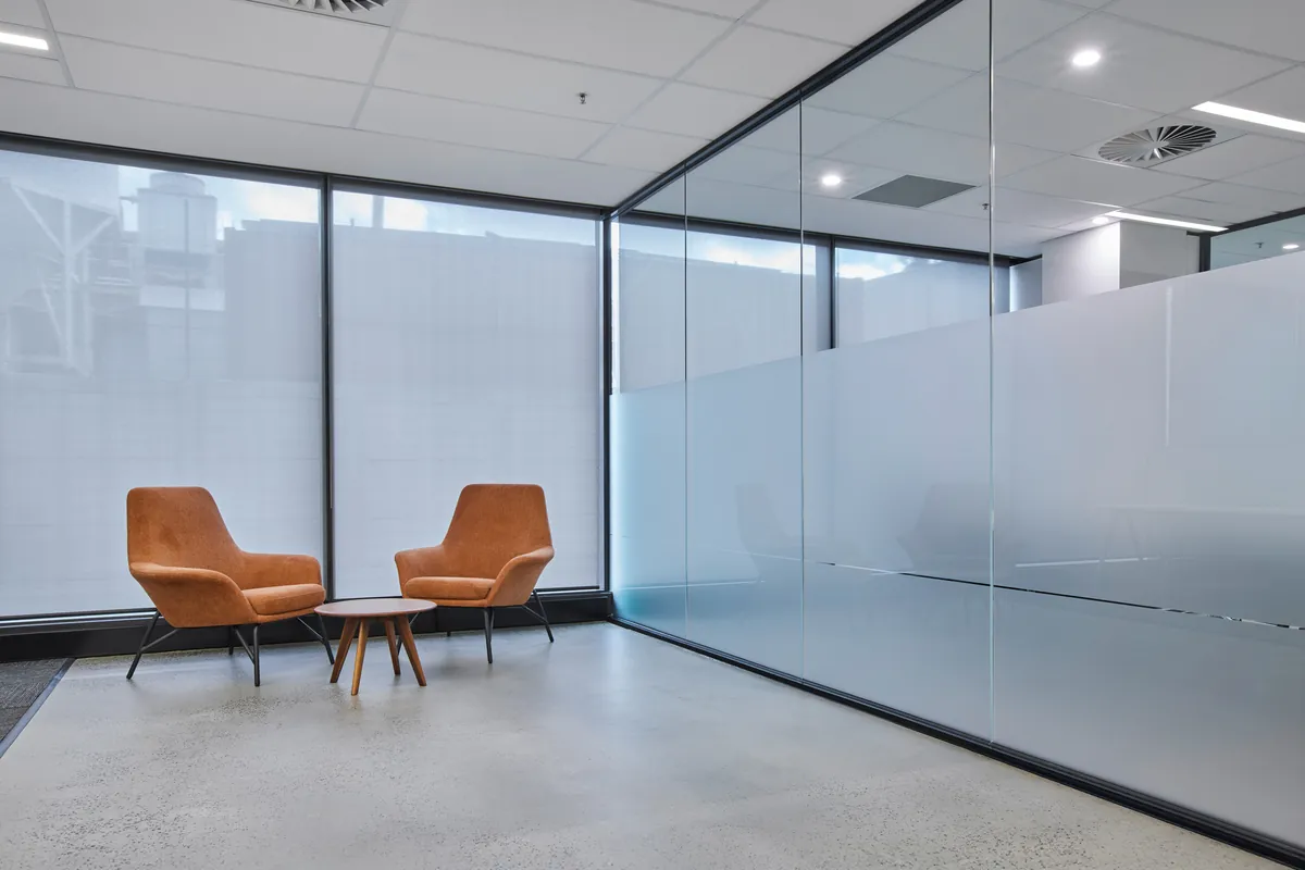 Breakout lounge with tan armchairs by full-height windows, Growthpoint spec suite fitout, Mulgrave.