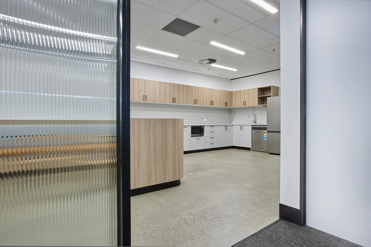 Kitchen with timber and white joinery viewed through a fluted glass doorway, Growthpoint spec suite fitout, Mulgrave.