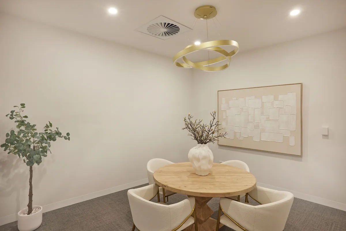 Consult room with round timber table, lounge chairs and feature pendant at the Kew Periodontics dental clinic fitout, Kew.