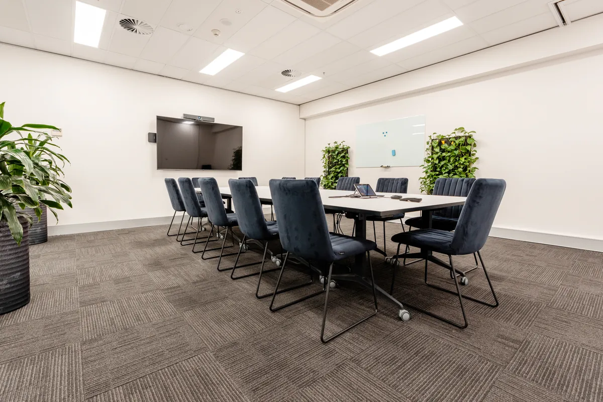 Boardroom with long table, velvet chairs, screen and biophilic green walls at the McLarens office fitout, Melbourne.