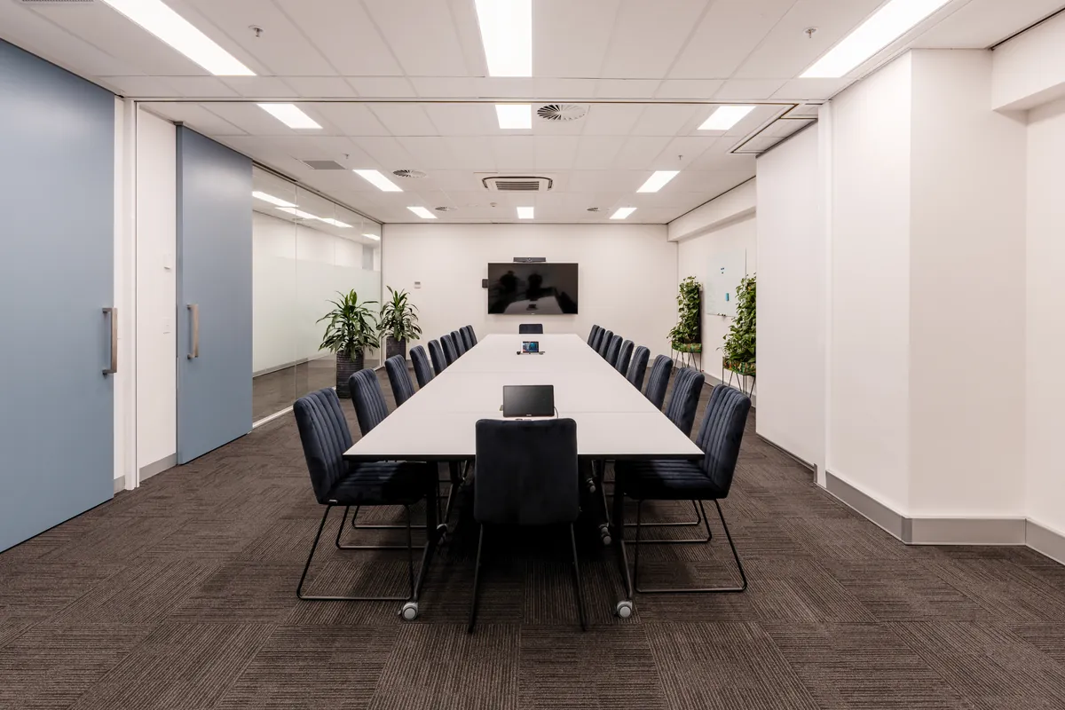 Boardroom with long conference table, leather chairs and wall-mounted screen at the McLarens office fitout, Melbourne.