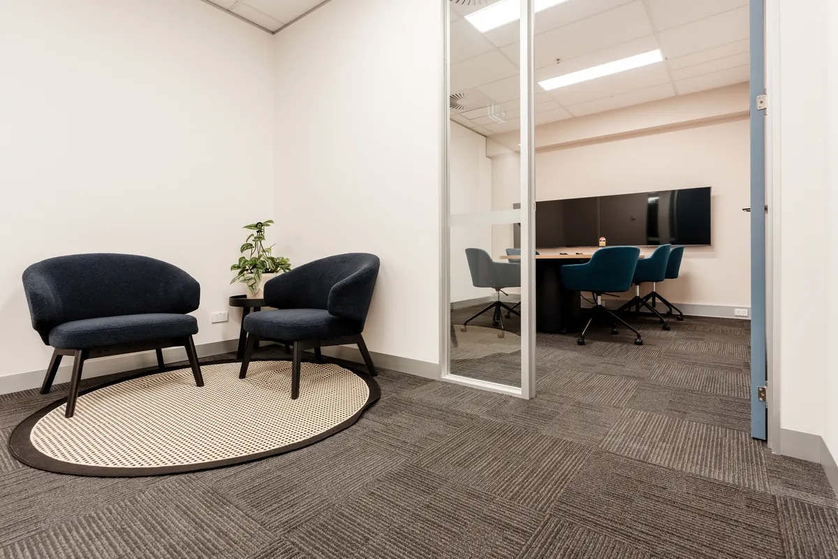 Soft seating nook beside a glass-partitioned meeting room at the McLarens office fitout, Melbourne.