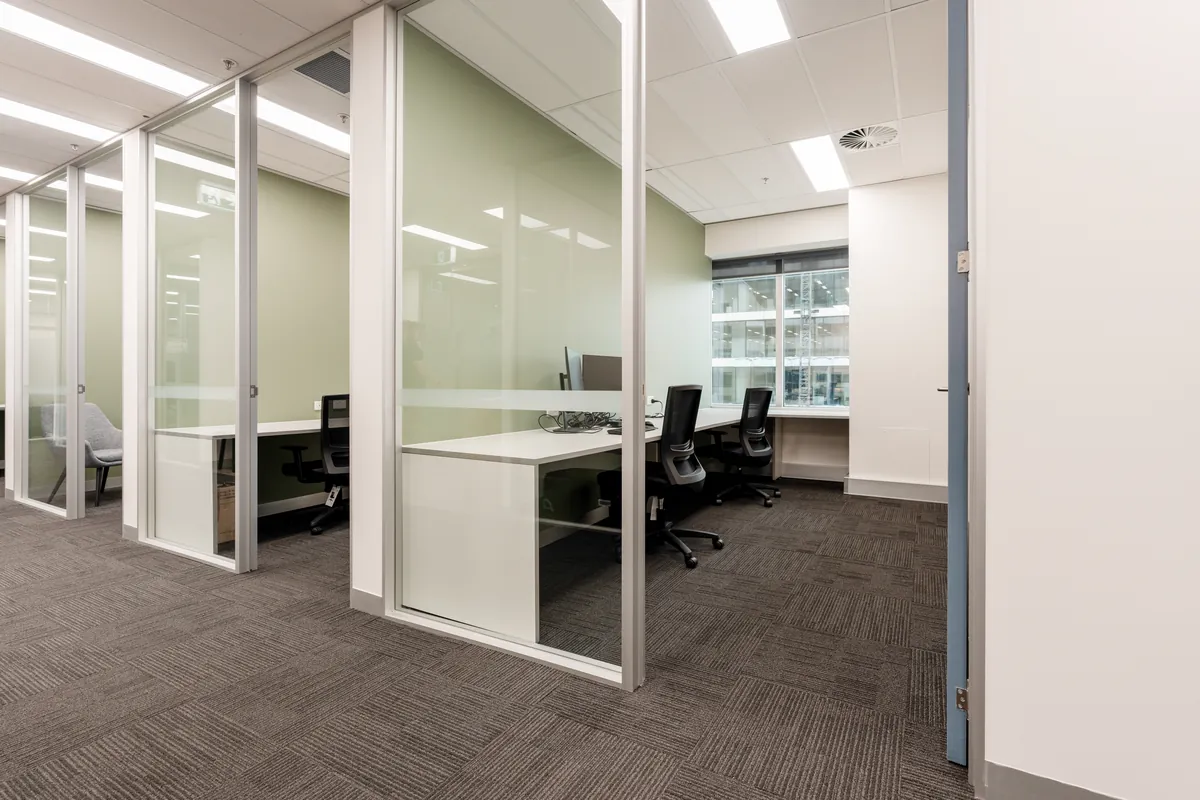 Glass-partitioned private offices with workstations and green accents at the McLarens office fitout, Melbourne.