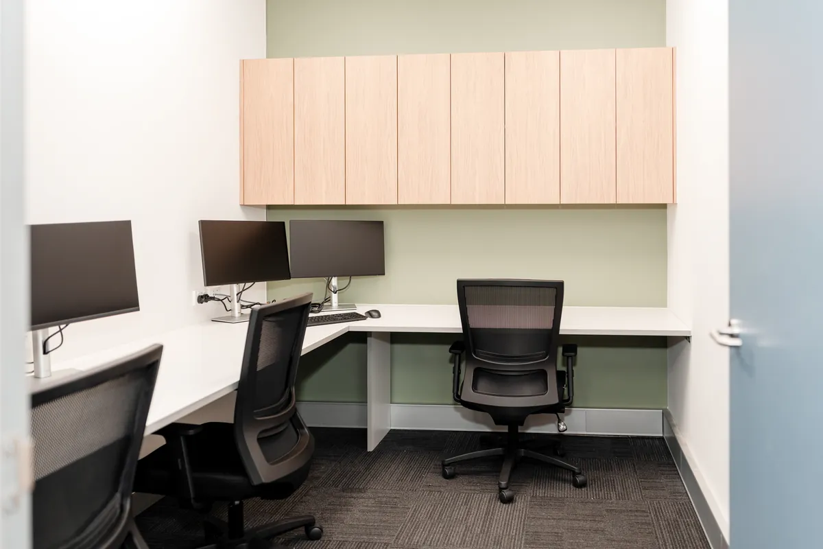 Two-person private office with corner desks, dual monitors and overhead joinery at the McLarens office fitout, Melbourne.