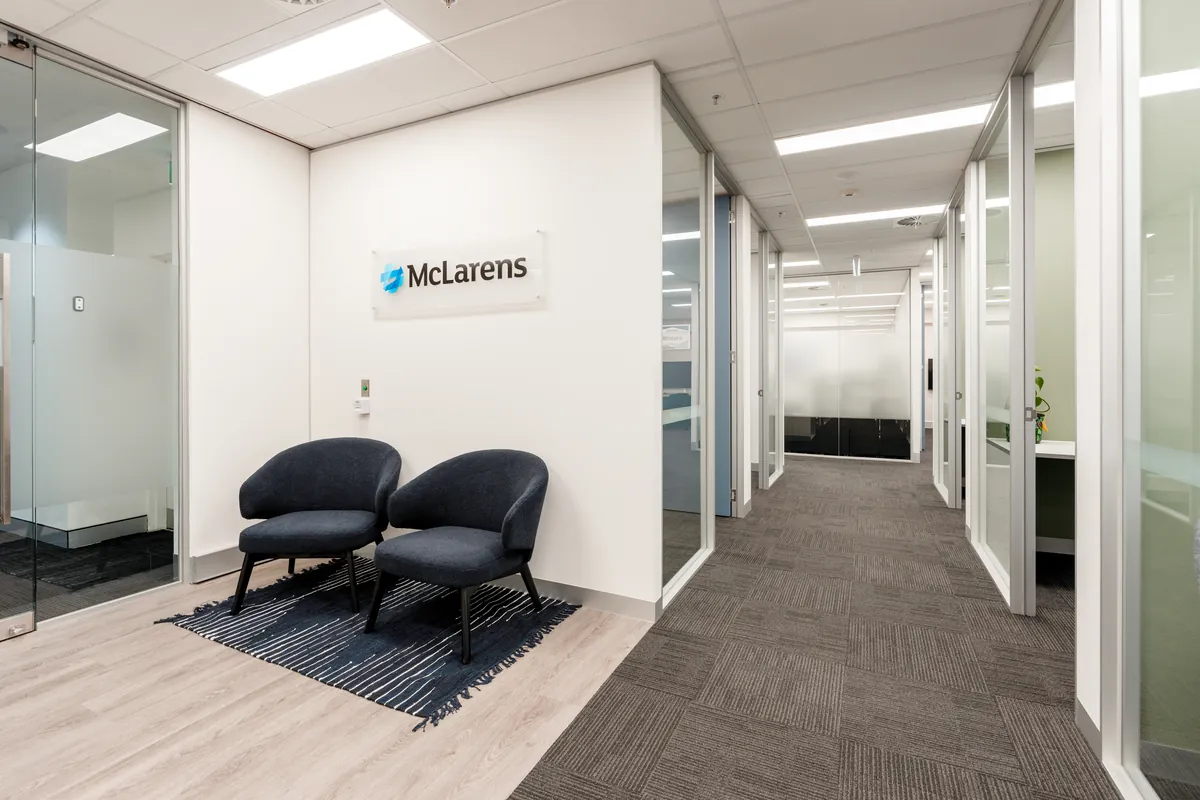 Branded reception with soft seating and glass-fronted office corridor at the McLarens office fitout, Melbourne.