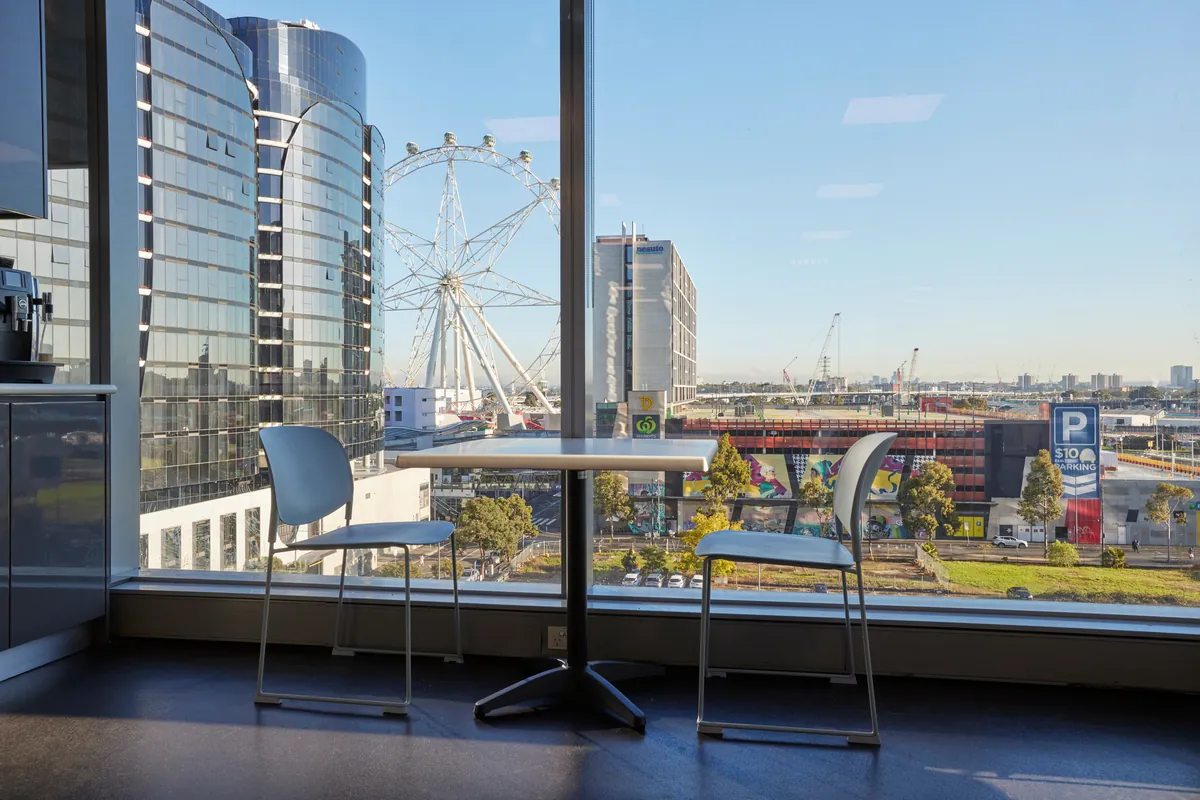 Kitchen breakout seating with floor-to-ceiling windows and city view at the Navantia office fitout, Docklands.