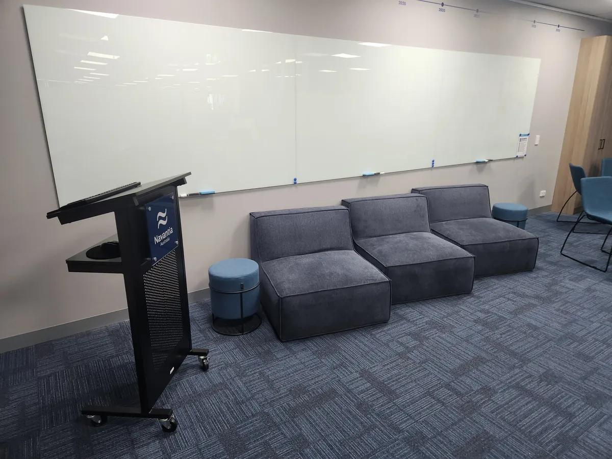 Training room with large glass whiteboard, lectern and modular sofa at the Navantia office fitout, Docklands.