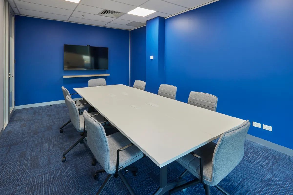 Meeting room with wall-mounted screen and blue feature wall at the Navantia office fitout, Docklands.
