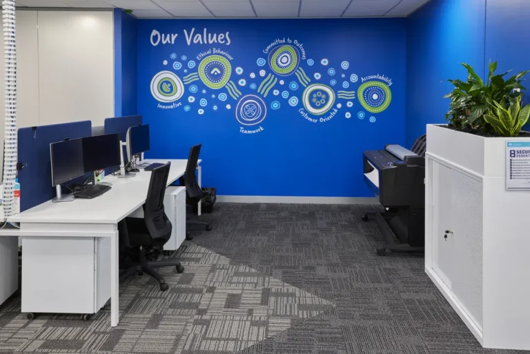 Workstations beneath a blue Our Values feature wall at the Navantia office fitout, Docklands.