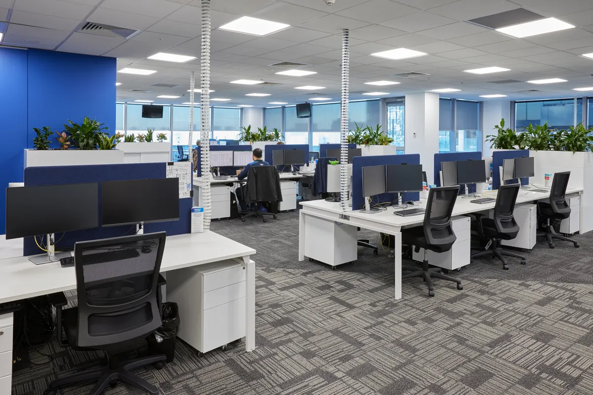 Open-plan workstations with acoustic screens and planters at the Navantia office fitout, Docklands.