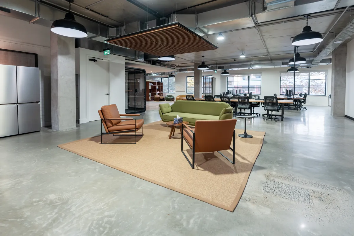 Breakout lounge with sofas and armchairs beside open-plan workstations, Resilience Project office fitout, Collingwood.