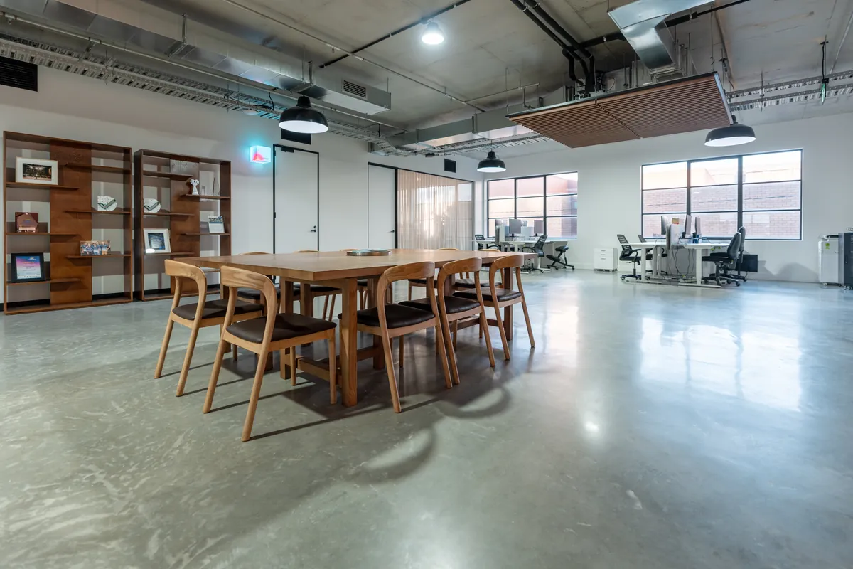 Open-plan workspace with communal table and workstations by large windows, Resilience Project office fitout, Collingwood.