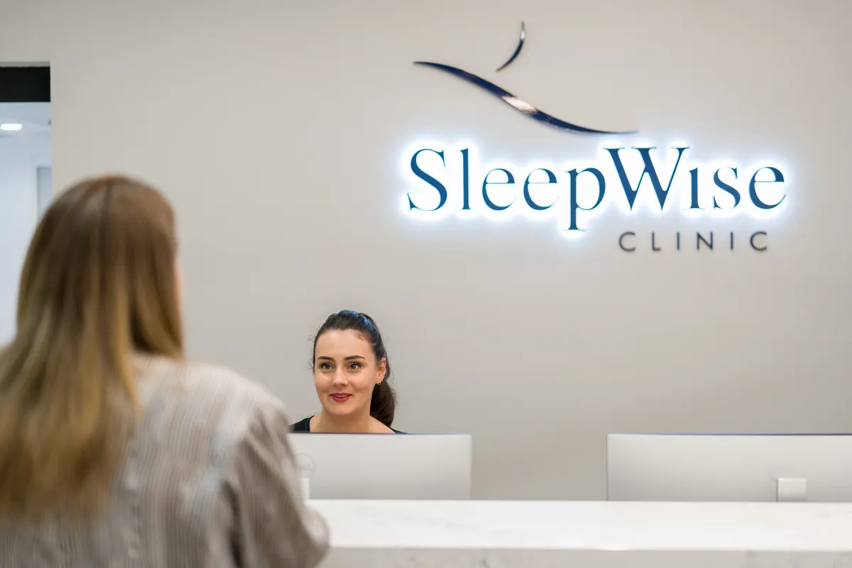 Receptionist greeting a patient beneath backlit signage at the SleepWise Clinic dental clinic fitout, Melbourne.